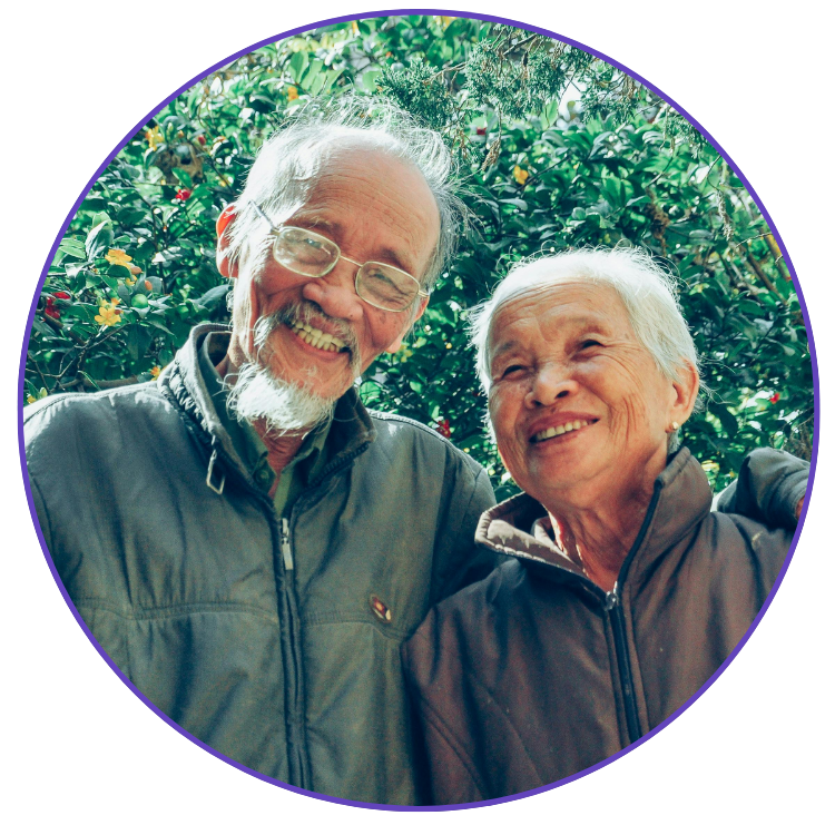 An older couple stood in front of a bush smiling