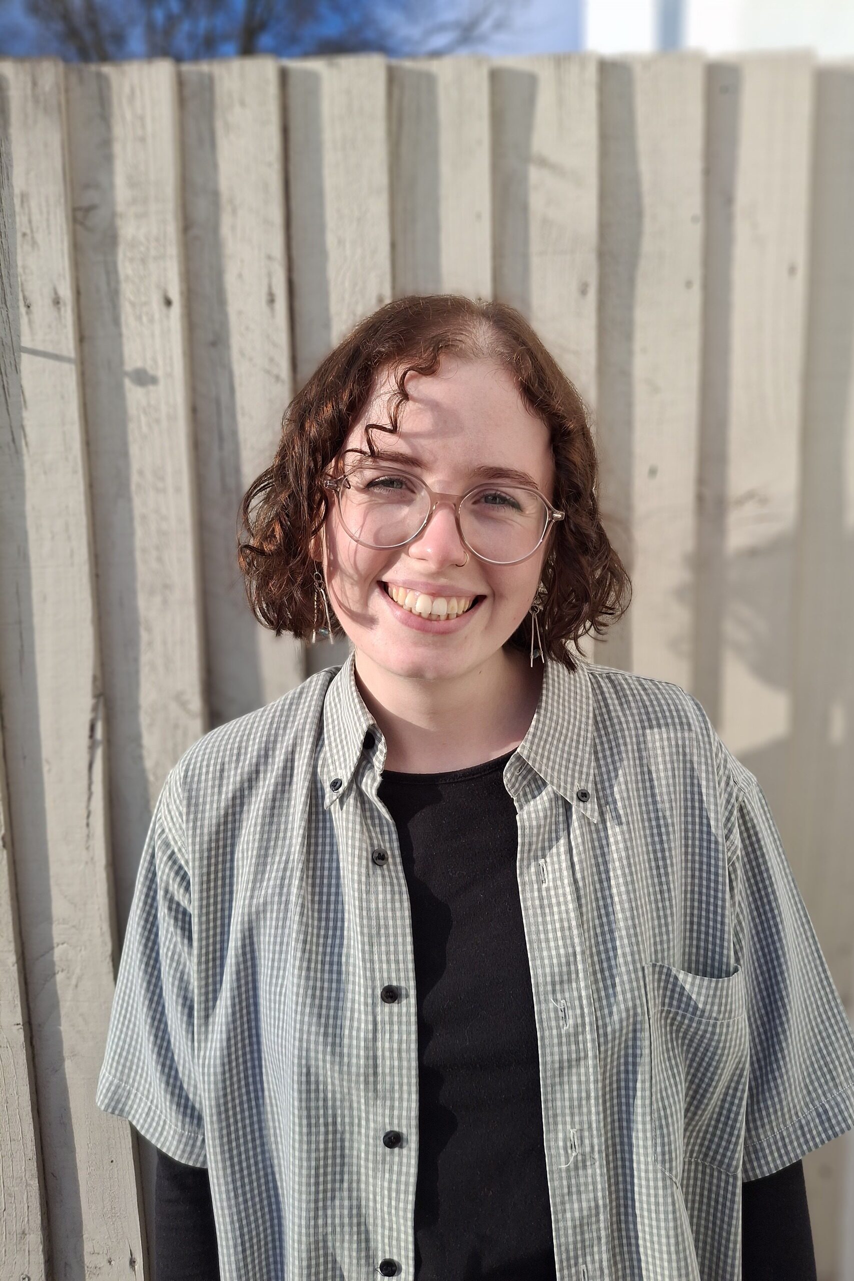 A photo of Nancy smiling at the camera. She is stood in front of a fence.